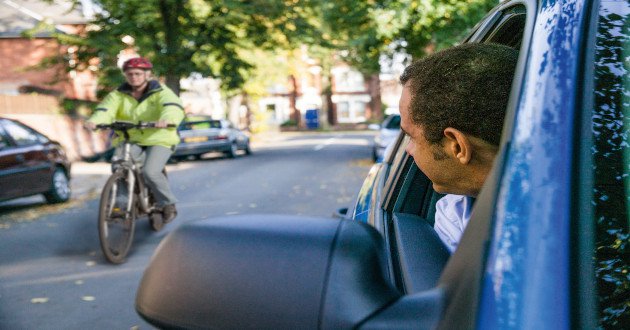 Driver with head out of window seeing passing cyclist in their blind-spot.