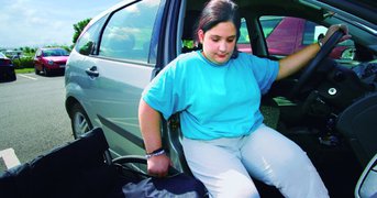 Disabled female driver manoeuvres herself between her vheicle and wheel chair.
