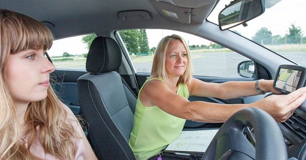 Instructor demonstrating sat nav control to leaner driver.