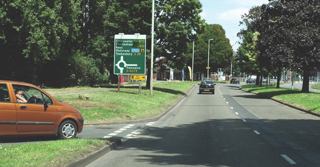 A car waits to emerge from slip road in a town, summer's day.