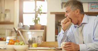 Tired male yawns at breakfast table before working day.