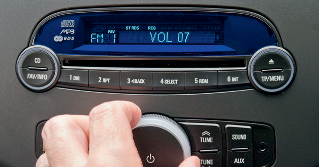 Close up of car stereo with hand adjusting volume dial.